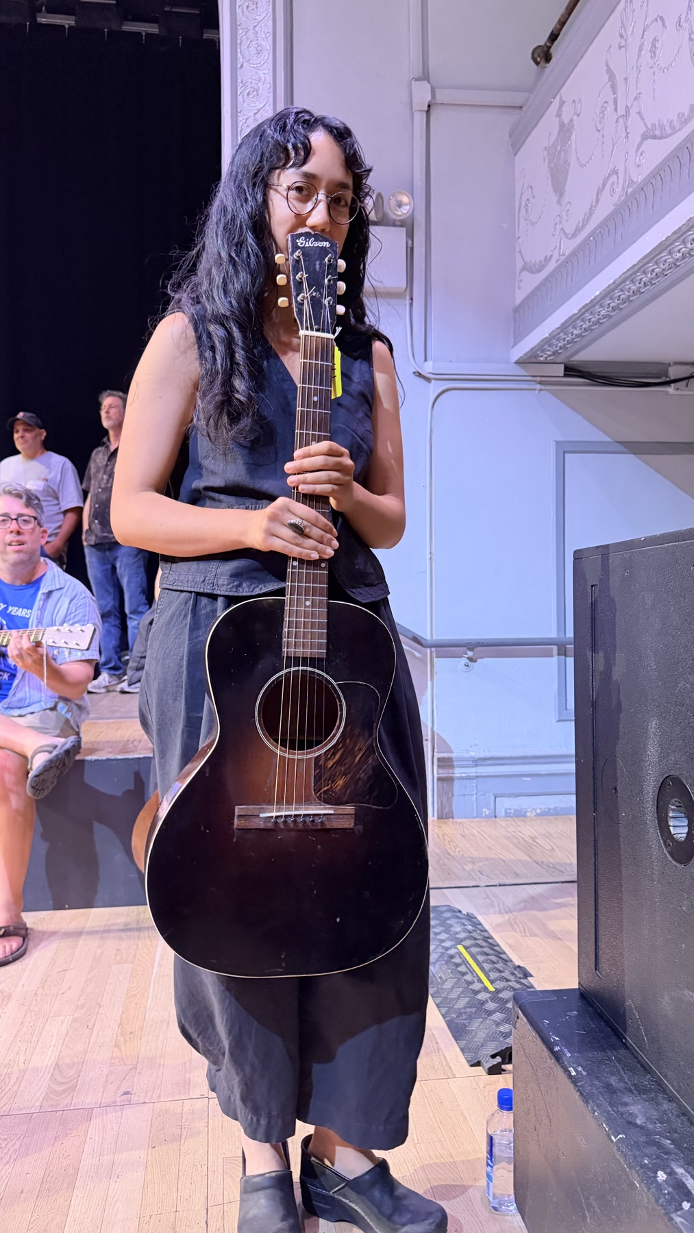A woman holding a vintage Gibson acoustic guitar onstage at Brooklyn Guitar Feast III.